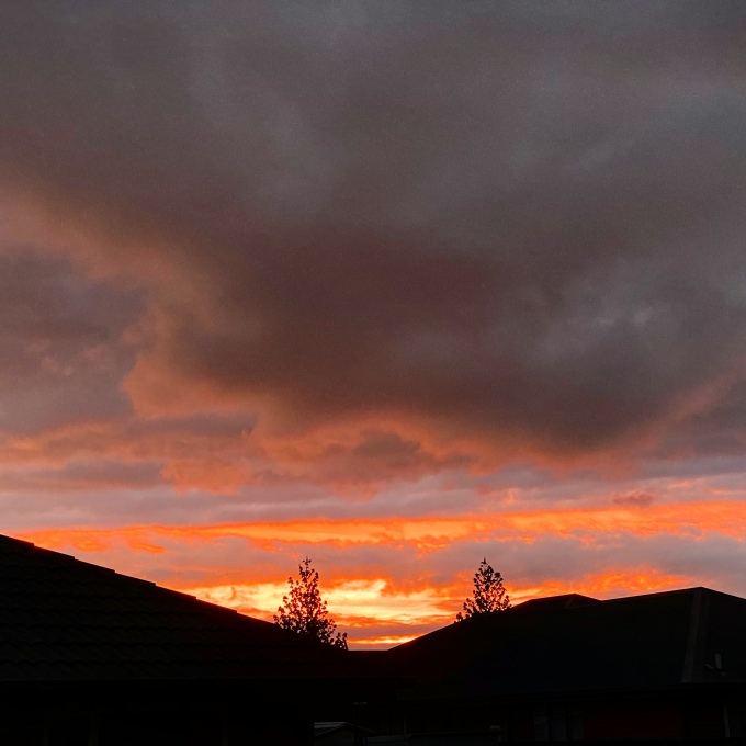 Sunset with orange and salmon tones in the gray clouds with roofs of houses in the background