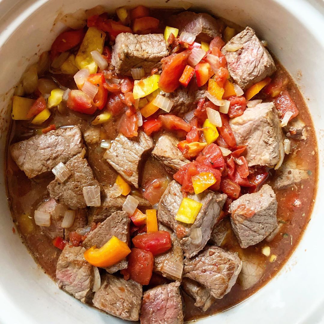 Cooked beef cubes, tomatoes, yellow peppers, onions, and a sauce making pepper steak casserole in a crockpot